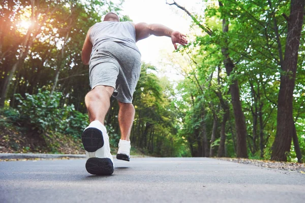 Outdoor cross-country running in concept for exercising, fitness and healthy lifestyle. Close up of feet of young runner man running along road in the park.