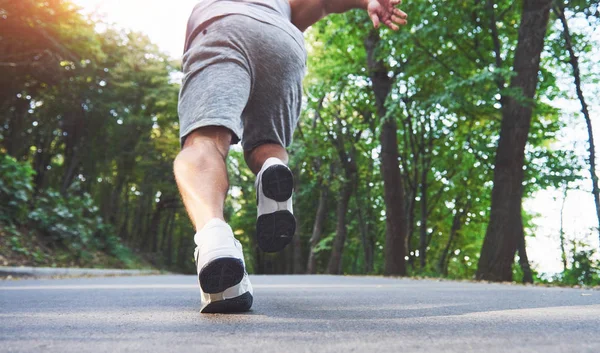 Outdoor cross-country running in concept for exercising, fitness and healthy lifestyle. Close up of feet of young runner man running along road in the park.