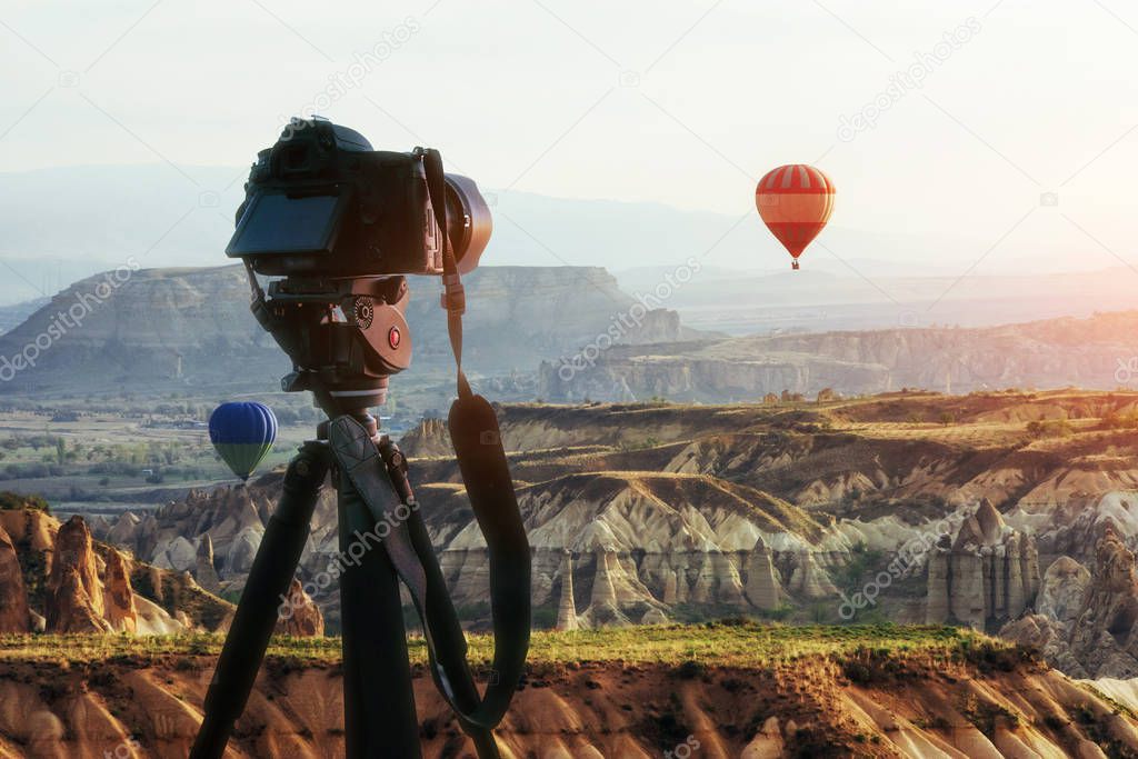 Hot air balloon flying over rock landscape at Turkey. DSLR camera on a tripod in the foreground. Cappadocia with its valley, ravine, hills, located between the volcanic mountains in Goreme National Park.