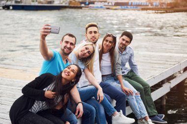 Bir grup genç iskelede oturuyor ve selfie çekiyorlar. Arkadaşlar gölde oyun oynuyorlar..