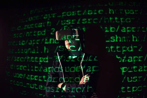 Double exposure of a caucasian man and Virtual reality VR headset is presumably a gamer or a hacker cracking the code into a secure network or server, with lines of code in green