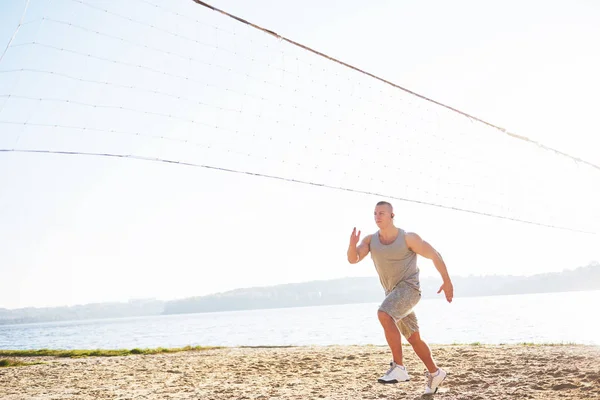 A athletic man looking at the seaside on the wild sand beach. Masculine and sporty male with naked torso is doing evening training at the sea cost. Summer work-out training outdoors.