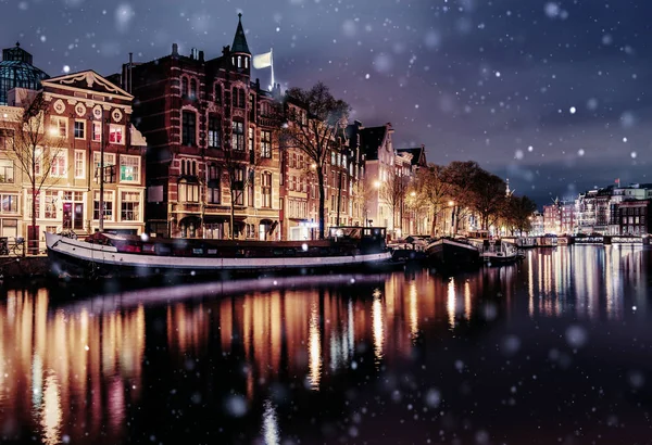 Beautiful night in Amsterdam. Night illumination of buildings and boats near the water in the canal during a snowstorm. Bokeh light effect, soft filter.