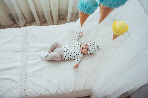 Newborn baby dressed in a white suit and black stars is a white soft bed in the studio.