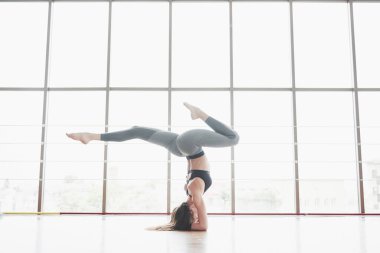 Yoga kursuna giden spor yapan bir kadın, bacaklarını büyük pencerenin yanında açıyor..