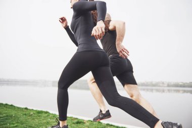 Couple jogging and running outdoors in park near the water. Young bearded man and woman exercising together in morning.