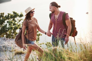 Sırt çantalı iki turist dağın tepesine tırmanıyor ve güneşin doğuşunun tadını çıkarıyor..