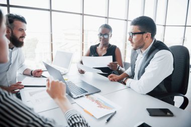 Ofiste dizüstü bilgisayarla oturan ve bir meslektaşını dinleyen şık bir bayan.