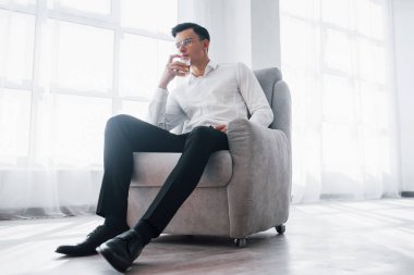 Dinlen ve sakinleş. Klasik giyinmiş, lüks görünümlü bir adam. Odadaki sandalyeye oturmuş, bardağı alkolle tutuyormuş..