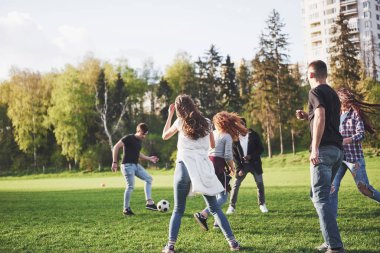 Gündelik kıyafetli bir grup arkadaş açık havada futbol oynuyor. İnsanlar eğleniyor ve eğleniyor. Aktif dinlenme ve manzaralı gün batımı.