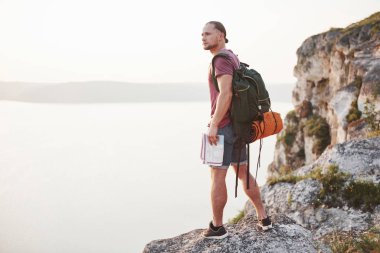 Haritası olan çekici bir adam su yüzeyinin üstündeki dağların manzarasının tadını çıkarıyor. Seyahat yaşam tarzı macera tatili konsepti.