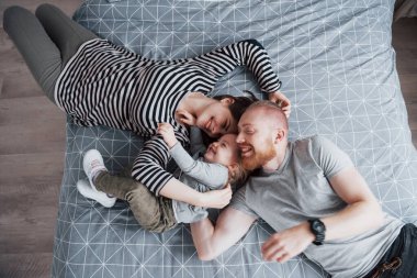 Güzel genç anne, baba ve onların kızı kameraya bakarak ve kafa kafaya yatakta yatıyordu süre gülümseyen Üstten Görünüm.