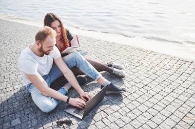 İki öğrenci erkek ve kız dışarıda oturuyor ve güneşli bir günde dışarıda laptopun keyfini çıkarıyorlar..