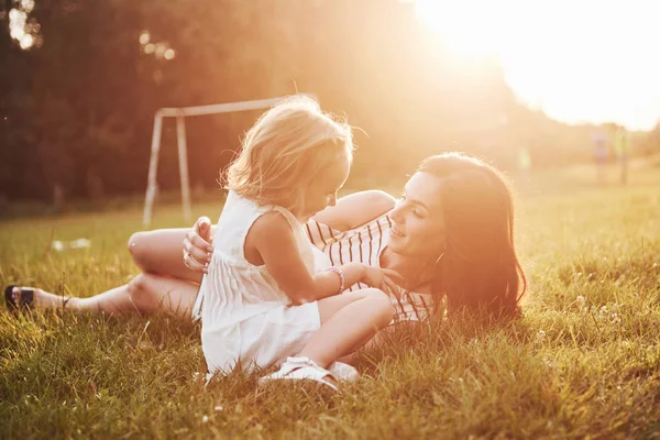 Mutlu anne ve kız güneşin altında bir parkta sarılıyorlar. Parlak bir yaz otlarının arka planında.