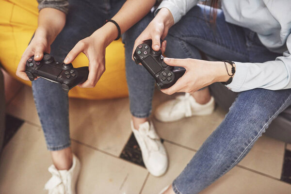 Twin sister sisters play on the console. Girls hold joysticks in their hands and have fun.