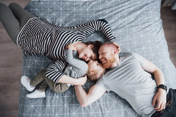 Güzel genç anne, baba ve onların kızı kameraya bakarak ve kafa kafaya yatakta yatıyordu süre gülümseyen Üstten Görünüm.