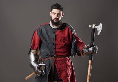 Gri arka planda ortaçağ şövalyesi. Zincirli zırhlı, kırmızı, siyah elbiseli ve savaş baltalı zalim, kirli yüzlü bir savaşçı portresi..
