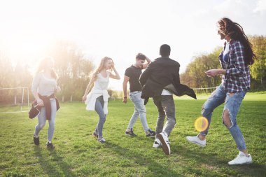 Gündelik kıyafetli bir grup arkadaş açık havada futbol oynuyor. İnsanlar eğleniyor ve eğleniyor. Aktif dinlenme ve manzaralı gün batımı.