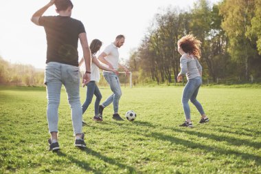 Gündelik kıyafetli bir grup arkadaş açık havada futbol oynuyor. İnsanlar eğleniyor ve eğleniyor. Aktif dinlenme ve manzaralı gün batımı.