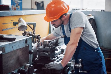 Büyük bir metal fabrikasında kasketli genç bir işçinin portresi. Makinelere hizmet eden mühendis, gaz ekipmanları için parça üretiyor..