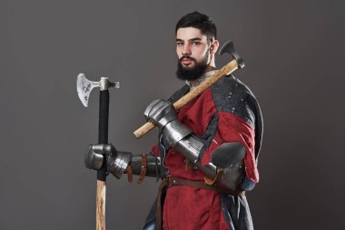 Gri arka planda ortaçağ şövalyesi. Zincirli zırhlı, kırmızı, siyah elbiseli ve savaş baltalı zalim, kirli yüzlü bir savaşçı portresi..