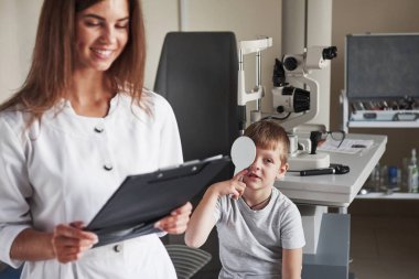 Bu süreçte gülümseyen bir kadın. Gözcü muayenehanesinde hamilelik testi yapıyorlar. Doktor verileri not eder.