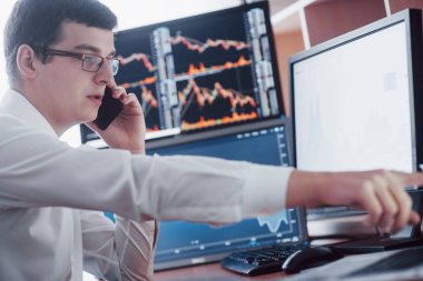 Telefondan sipariş alırken borsacıların online alım-satımları sayesinde. Arka planda dosya ve veri analizleriyle dolu çoklu bilgisayar ekranları.