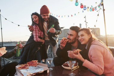 Birlikte olmak her zaman eğlencelidir. Çatıdaki partide pizza yiyorum. İyi arkadaşlar hafta sonları lezzetli yiyecekler ve alkolle vakit geçirir..