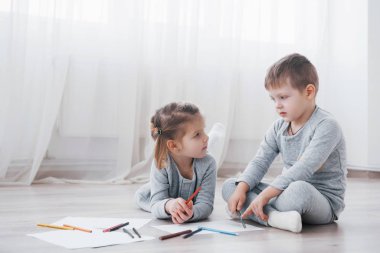 Çocuklar pijamalarıyla yere yatar ve kalemle çizerler. Kalemlerle resim yapan şirin bir çocuk..