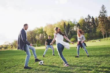 Gündelik kıyafetli bir grup arkadaş açık havada futbol oynuyor. İnsanlar eğleniyor ve eğleniyor. Aktif dinlenme ve manzaralı gün batımı.