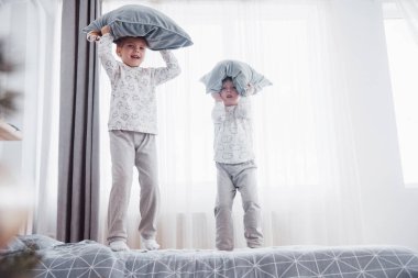 Beyaz yatak odasında oynayan mutlu çocuklar. Küçük çocuk ve kız kardeşi ve kız kardeşi pijama giymiş yatağa oynamak. Çocuklar için kreş iç. Kıyafeti ve yatak takımları bebek ve yürümeye başlayan çocuk için. Aile evde
