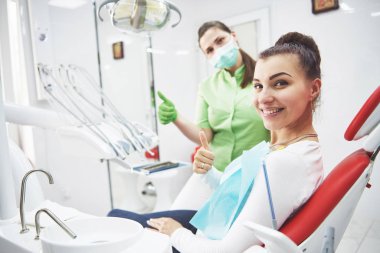 Genç bir kadın dişçinin işinden tatmin olur ve baş parmağını kaldırır..