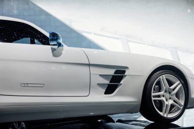Sağ mavi aynalı, dönüş sinyali, beyaz ışıklı alaşım tekerlekleri ve düşük profilli lastikleri olan modern, süslü spor arabanın yan görüntüsü, penceredeki ışıkların yansıması..
