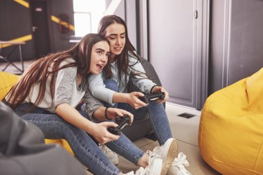 İkiz kız kardeşler konsolda oynarlar. Kızlar joystickleri ellerinde tutup eğleniyorlar..