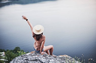 Feeling freedom and fresh air. Attractive tourist girl posing at the edge of mountain with clear water lake in background.