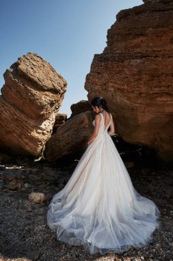 Sahilde fotoğrafçı pozu veren muhteşem gelinlikli bir kızın portresi. Gelin kayalıklarda.