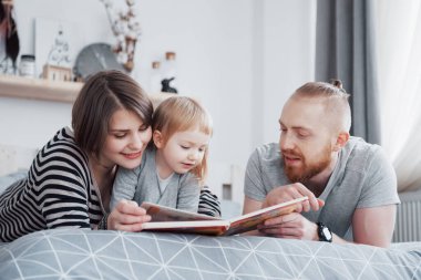 Baba, Anne ve Küçük Kız Oturma Odasında Çocuk Kitabı Okuyorlar. Mutlu büyük aile bayram gününde ilginç bir kitap okudu. Ebeveynler çocuklarını sever..
