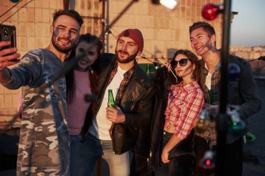 Bir grup pozitif arkadaş için selfie zamanı arkada duvarla çatıda duruyor..