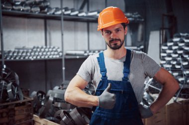 Büyük bir metal fabrikasında kasketli genç bir işçinin portresi. Shiftman bitmiş ürünlerin deposunda..