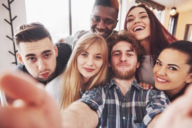 Arkadaşlar restoranda eğleniyor. İki erkek ve dört kız selfie çekiyor, barış işareti yapıyor ve gülüyorlar. Ön plandaki kadının elinde akıllı telefon var. Herkes günlük kıyafetler giyer..