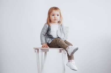 Küçük bir kız taburede oturuyor. Mutlu çocukluk kavramı. Beyaz arkaplanda izole