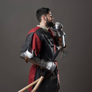 Gri arka planda ortaçağ şövalyesi. Zincirli zırhlı, kırmızı, siyah elbiseli ve savaş baltalı zalim, kirli yüzlü bir savaşçı portresi..