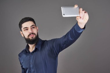 Yenilikçi iş adamı selfie fotoğraf gülümseyen ve telefon gri studio arka plan bakarak akıllı telefon ile konuşurken Genç sakallı.