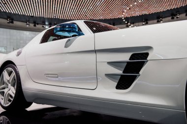 Sağ mavi aynalı, dönüş sinyali olan modern spor arabanın yan görüntüsü, beyaz ışıklı alaşımlı tekerlekler ve düşük profilli lastikler, pencerelerdeki ışıkların yansıması.