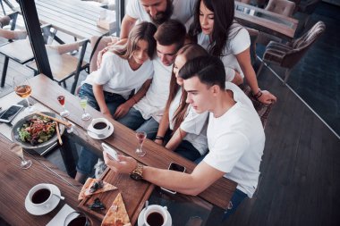 Bir grup insan bir kafede selfie çekiyor. En iyi arkadaşlar yemek masasında toplanmış pizza yiyor ve çeşitli içkiler söylüyorlardı..