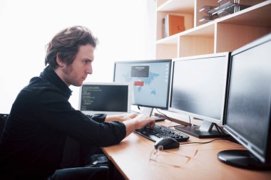 Genç tehlikeli hacker, hassas verileri indirerek ve virüsleri etkinleştirerek devlet hizmetlerini bozuyor. Bir adam birçok monitörü olan bir dizüstü bilgisayar kullanır..