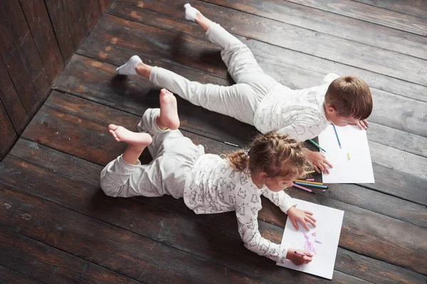 Children lie on the floor in pajamas and draw with pencils. Cute child painting by pencils.