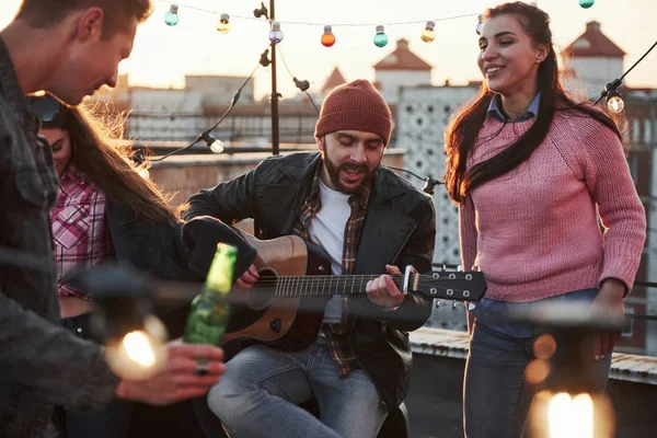 Müzik aleti çalmak her zaman iyi bir beceridir. Gitarist çatıdaki arkadaşları için dekoratif renkli ampullerle oturup şarkı söylüyor..