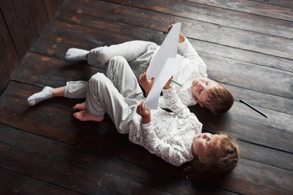 Children lie on the floor in pajamas and draw with pencils. Cute child painting by pencils.