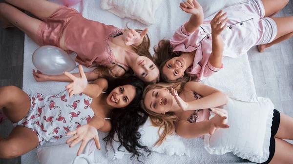Air kisses. Top view of young girls at bachelorette party lying on the sofa and raising their hands up.